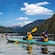 4 kayakers paddling through waters surrounded by forest and snowcapped mountains